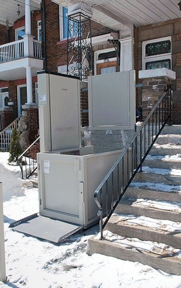 Access porch lift installed outdoors covered with a light layer of snow during winter, providing safe accessibility despite cold weather.