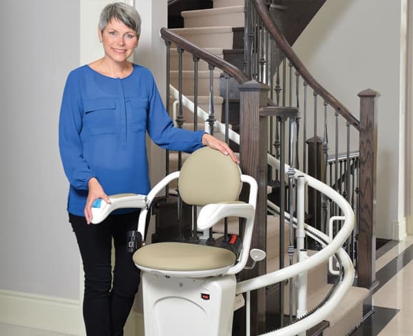 Lady Standing by Stairs with a Curved Stairlifts in Naperville, IL, Kenosha, Lake Geneva, Racine, Chicagoland, Downers Grove, IL