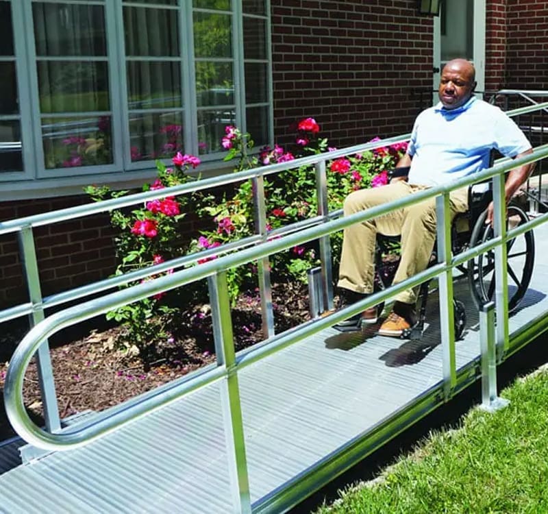 Man in wheelchair safely descending an aluminum wheelchair ramp with handrails installed by Access Elevator, Inc.