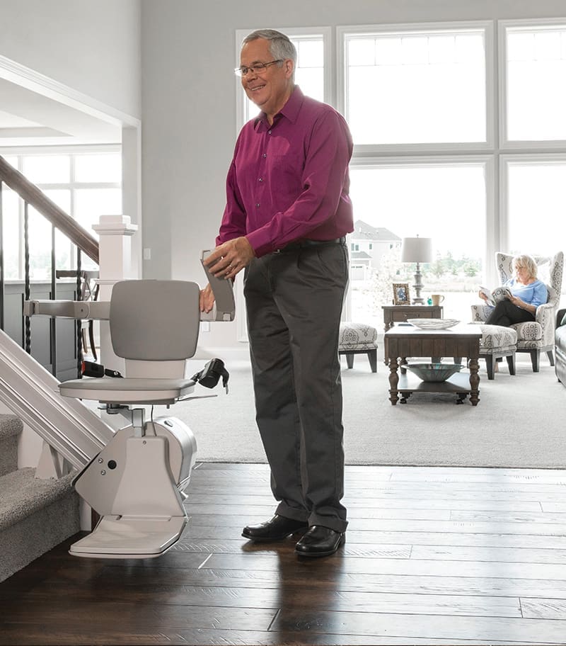 Elan-Straight-Indoor-Stair-Lift-09 Owner Demonstrating Ease of Folding Up Armrest on Bruno Elan Straight Stairlift at Bottom of Stairs