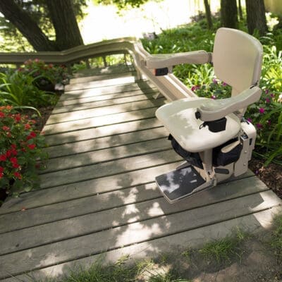 Bruno Elite Outdoor Curved Stairlift On Wood Deck With Plants in Background, Showing Curved Portion of Rail in Distance