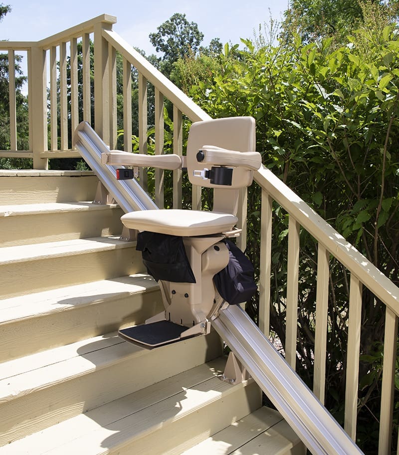 Bruno Elite Heavy Duty Outdoor Stair Lift Halfway Up Wood Deck in Unfolded Position with Green Plants in Background