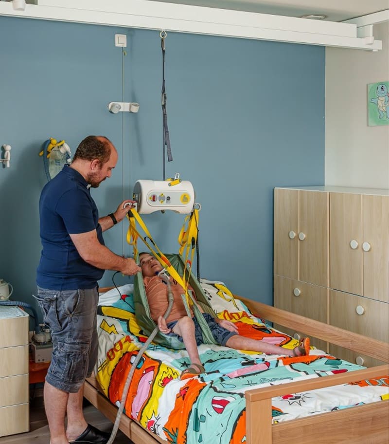 Access-Surehands-Portable-Ceiling-Lift-System-02 Father helping disabled son to bed with SureHands portable ceiling lift and sling