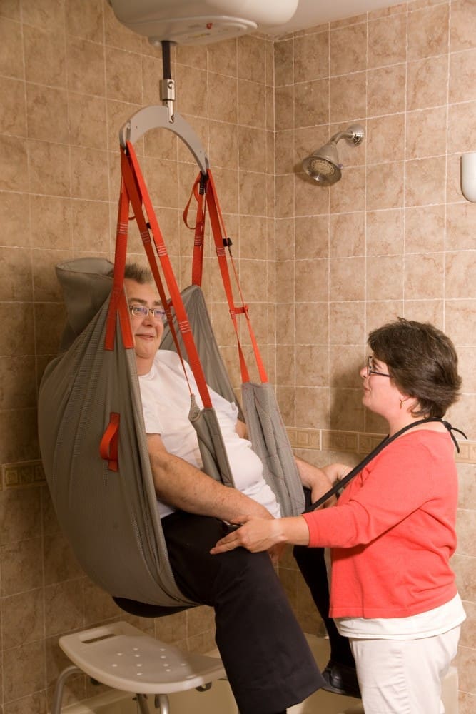 Caregiver using SureHands Bariatric Ceiling Lift and Sling to easily and safely assist in patient transfer to shower