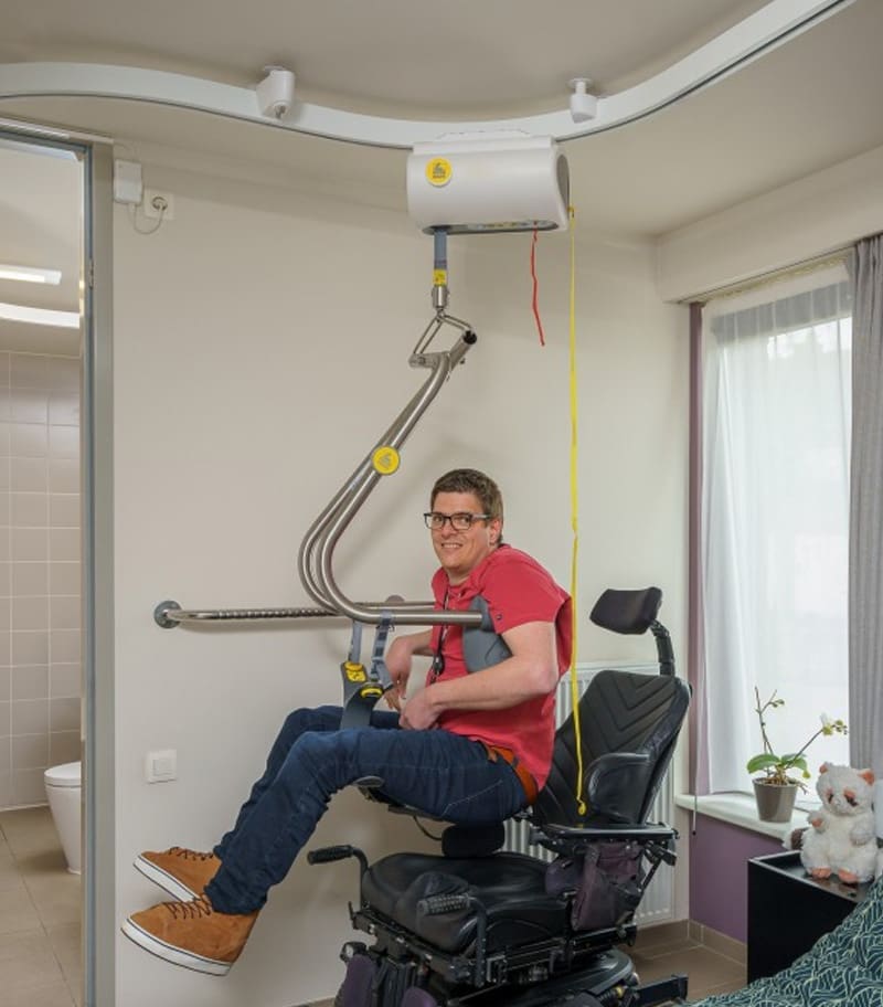 Client using ceiling lift with Body Support Harness from SureHands for independent transfer into power chair