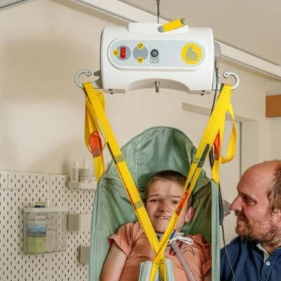 Happy child with caregiver using a portable SureHands ceiling lift and sling for safe transfer.