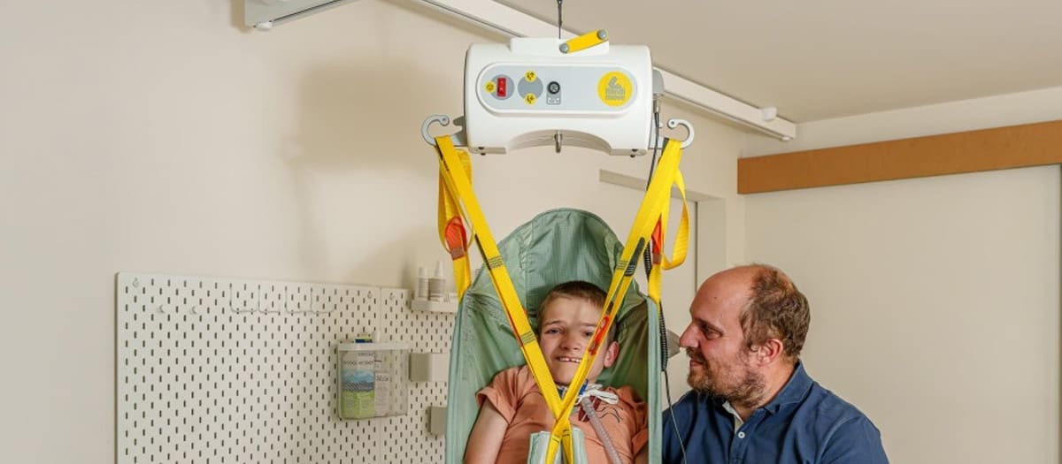 Happy child with caregiver using a portable SureHands ceiling lift and sling for safe transfer.